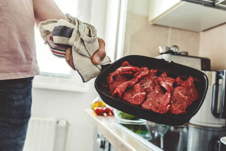 Young man cooking meat on grill pan at home in the kitchen.の写真素材