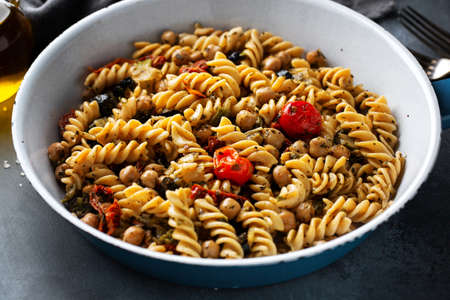 Tasty appetizing vegan pasta with vegetables and chickpeas cooked and served on pan. Closeup.