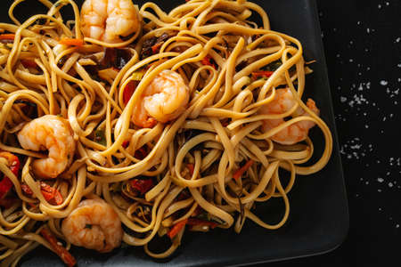 Tasty appetizing noodles with shrimps and vegetables served on black plate. Closeup.の写真素材