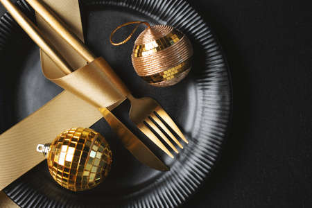 Christmas golden cutlery on plate with bauble and ribbon on dark background.