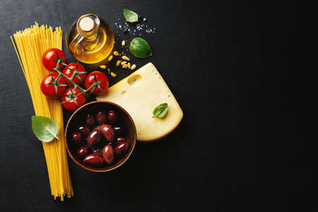 Traditional italian food background with spaghetti tomatoes cheese olives and oil on dark background.の写真素材