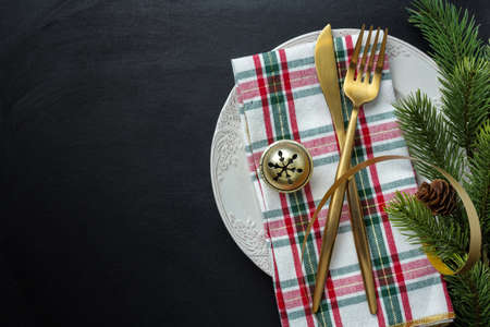 Christmas golden cutlery on plate with ribbon on dark background.