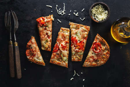 Small pizza pieces with cheese on dark background. View from above.