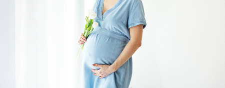 Pregnant woman holding spring flowers. Lifestyle. Maternity holiday concept. Banner.の写真素材