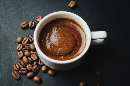 Tasty steaming espresso in cup with coffee beans. Closeup. Dark background.