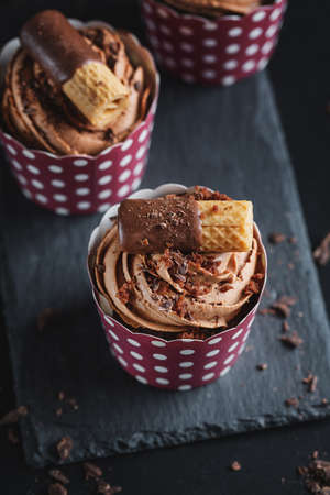 Tasty chocolate muffins cupcakes with buttercream decorated in cups on dark background. Closeupの写真素材