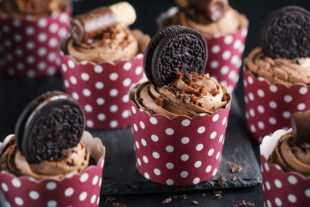 Tasty chocolate muffins cupcakes with buttercream decorated in cups on dark background. Closeupの写真素材