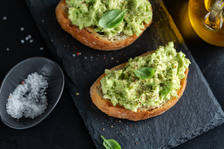 Tasty appetizing toast with mashed avocado served on dark board.