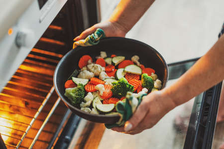 Woman cooking vegetables puting pan with vegetables to the oven. Home cooking concept.の写真素材