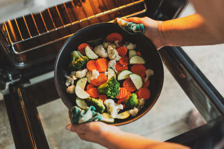 Woman cooking vegetables puting pan with vegetables to the oven. Home cooking concept.の写真素材