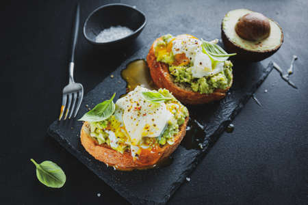 Tasty appetizing toast with avocado and egg served on dark board.の写真素材