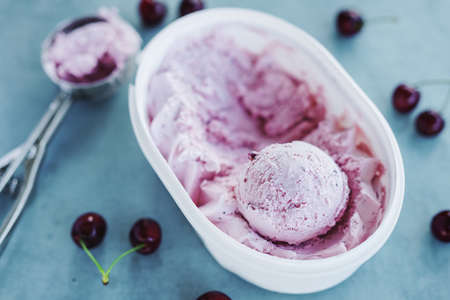 Tasty refreshing ice cream with cherry in plastic box on bright background.