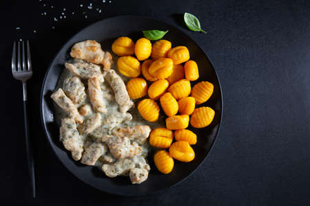 Sweet potato gnocchi with chicken in sauce served on dark plate on dark background.の写真素材