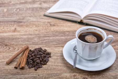 A cup of coffee and cinnamon with a book on a wooden backgroundの写真素材