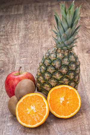 Orange oranges, pineapple, kiwi and apple on a brown wooden backgroundの写真素材