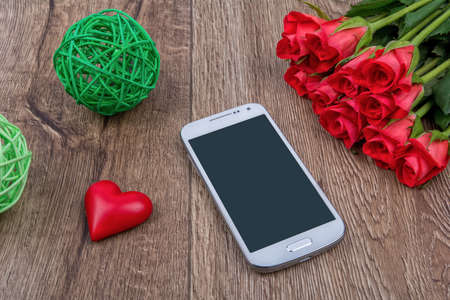 Mobile phone, red heart and red roses on a wooden backgroundの写真素材