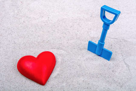 Red heart and blue scoop on a grey sand backgroundの写真素材
