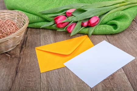Envelope with sheet of paper and red tulips on a wooden background