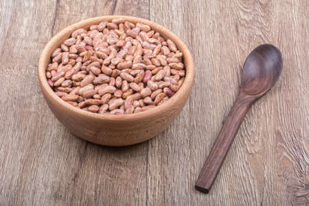 Bowl with beans and wooden spoon on a brown wooden backgroundの写真素材