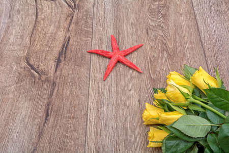 Red starfish and yellow roses on a wooden background