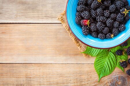 Fresh blackberries in blue ceramic bowl and leaves on wooden background in rustic style. Top view.の写真素材