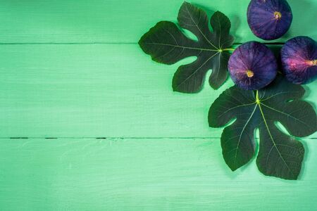 Fresh figs with leaves on green wooden background. Top view.
