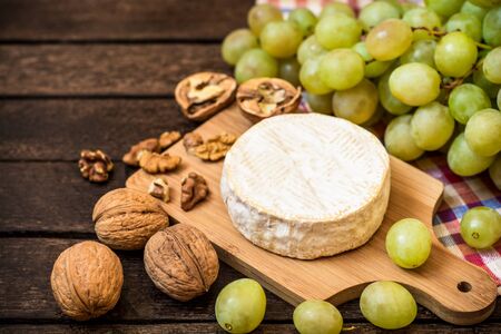 Camembert cheese with walnuts and green grapes on wooden rustic background. Selective focus.の写真素材