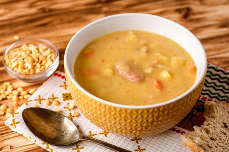 Split pea soup with meat, potatoes and carrots in ceramic bowl on wooden background. Rustik style. Selective focus.の写真素材