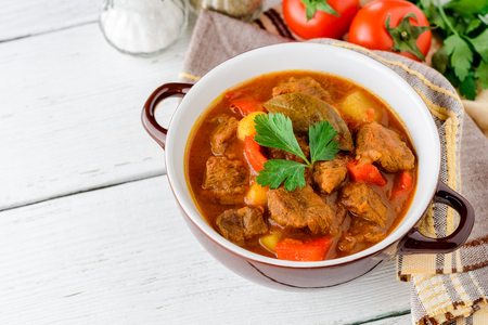 Goulash in ceramic bowl on white wooden background. Traditional hungarian soup. Rustic style. Selective focus.の写真素材