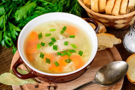 Homemade chicken soup with noodles and vegetables in ceramic bowl on wooden table. Selective focus.の写真素材