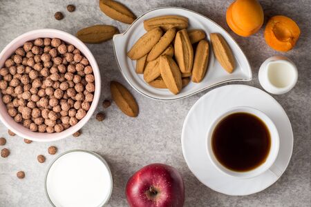 Breakfast table with coffee, ginger cookies, chocolate cereal balls, milk and fruits on stone background. Top view.の写真素材