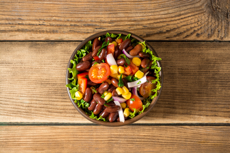 Fresh vegetable salad with beans in ceramic bowl on wooden table. Healthy vegetarian food. Top view and copy space.の写真素材