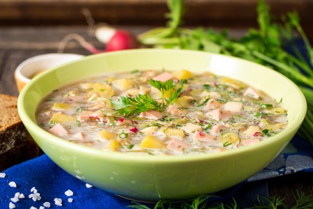 Okroshka. Traditional Russian summer cold soup with sausage, vegetables and kvass in bowl on wooden background. Selective focus.の写真素材
