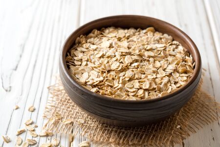 Oat flakes in ceramic bowl on white wooden table. Selective focus.