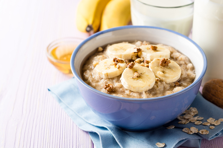 Oatmeal porridge with banana, walnuts and honey in bowl on purple wooden background. Healthy breakfast. Selective focus.の写真素材
