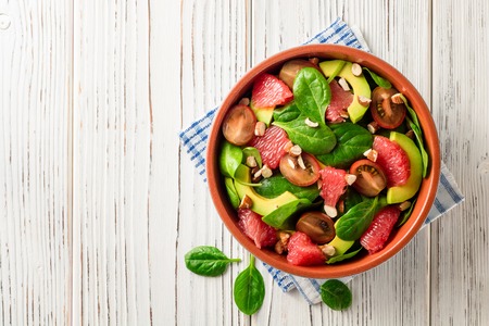 Fresh salad with spinach, avocado, tomatoes, grapefruit and almonds on white wooden background. Top view. Copy space.の写真素材