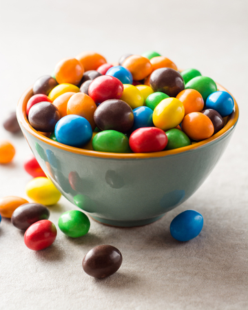 Colorful chocolate buttons in bowl on gray stone background. Selective focus.の写真素材