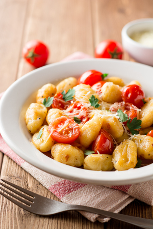 Homemade italian gnocchi with tomato, garlic, parsley and parmesan cheese on wooden table. Selective focus.の写真素材