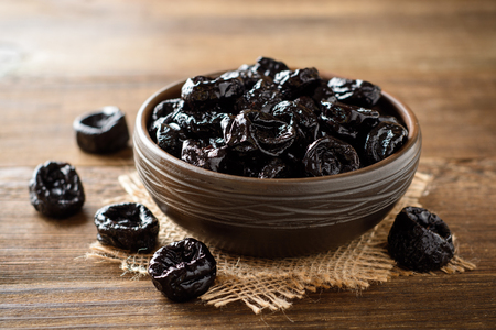 Prunes in ceramic bowl on rustic wooden table. Dried plums. Selective focus.の写真素材