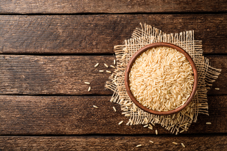 Raw brown rice in ceramic bowl on dark rustic wooden background. Top view. Copy space.の写真素材
