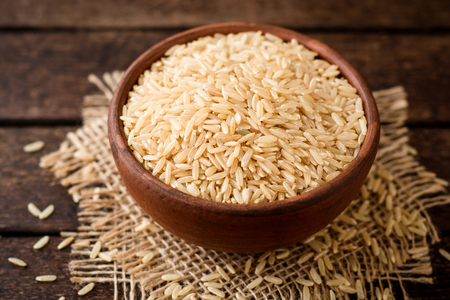 Raw brown rice in ceramic bowl on dark rustic wooden background. Selective focus.の写真素材