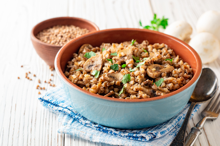 Buckwheat porridge with mushrooms in a bowl on white wooden background. Selective focus.の写真素材