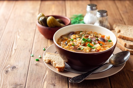 Traditional Russian soup Rassolnik with pickled cucumbers and pearl barley in bowl on wooden table. Selective focus.の写真素材