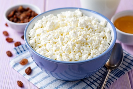 Cottage cheese in blue bowl on purple wooden background. Selective focus.の写真素材
