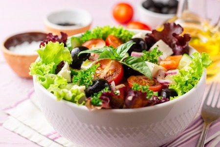Fresh Greek salad with vegetables, feta cheese and black olives in white bowl on purple wooden background. Selective focus.の写真素材
