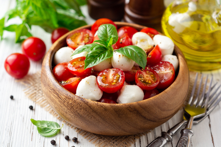 Italian caprese salad with cherry tomatoes, mozzarella cheese and basil on white wooden background. Selective focus.の写真素材