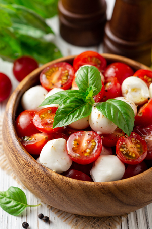 Italian caprese salad with cherry tomatoes, mozzarella cheese and basil on white wooden background. Selective focus.の写真素材