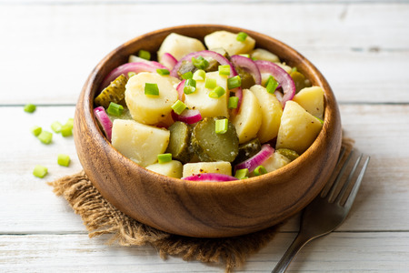 Potato salad with pickled cucumbers and onion in bowl on white wooden table.の写真素材