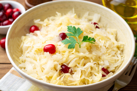 Sauerkraut with cranberries and parsley in bowl on wooden table. Selective focus.の写真素材