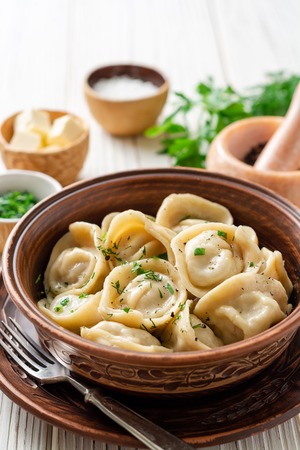Traditional russian homemade meat dumplings pelmeni with butter and greens in ceramic bowl on white wooden table. Selective focus.の写真素材
